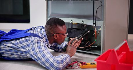 Um homem está deitado no chão consertando uma geladeira.